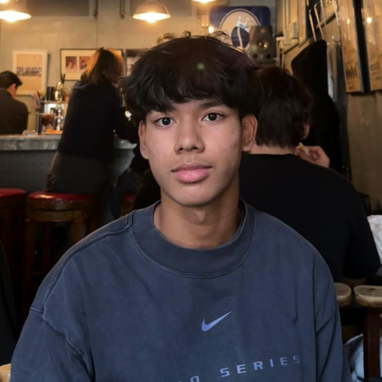 Young man with dark hair in a casual blue Nike sweatshirt in a cafe setting.