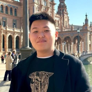 Young man smiling outdoors in front of historic architecture in daylight.