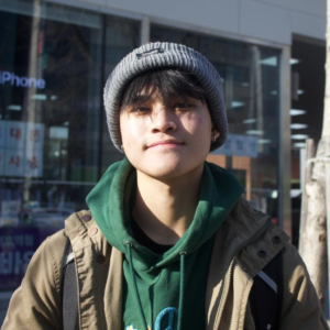 Young man wearing a grey beanie and green hoodie outdoors in sunlight.