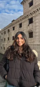 Smiling young woman with long dark hair in front of historic stone building.