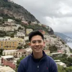 Young man smiling with hillside cityscape in the background.