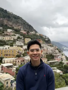 Young man smiling with hillside cityscape in the background.