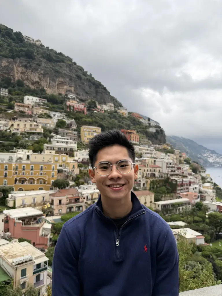 Young man smiling with hillside cityscape in the background.