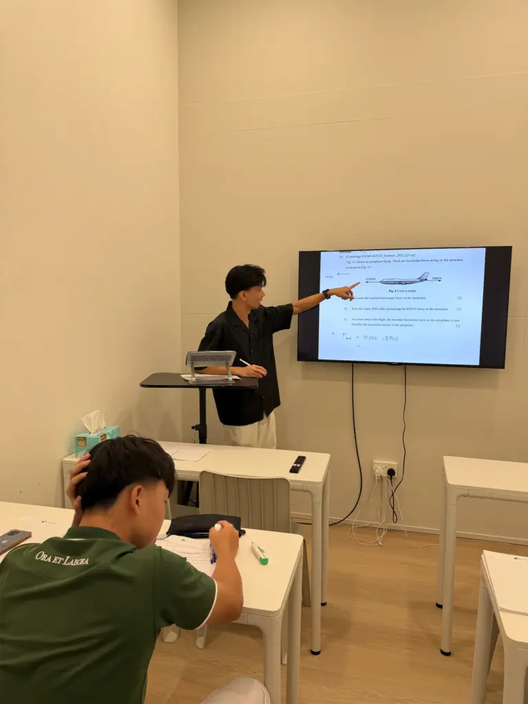 Teacher explaining physics concepts on a digital screen in a classroom.