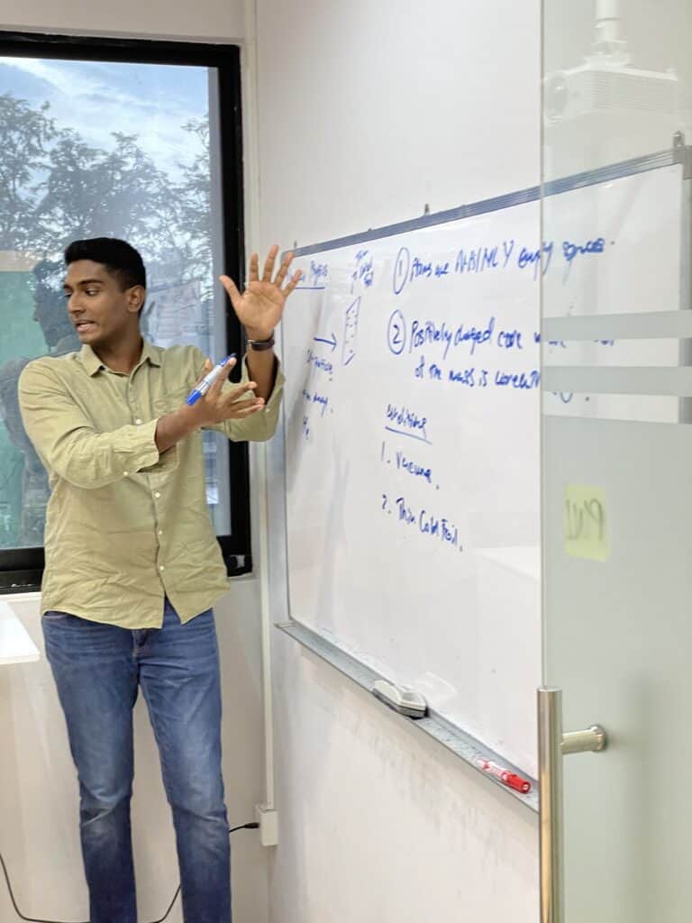 Young male student explaining physics concepts on whiteboard in classroom.