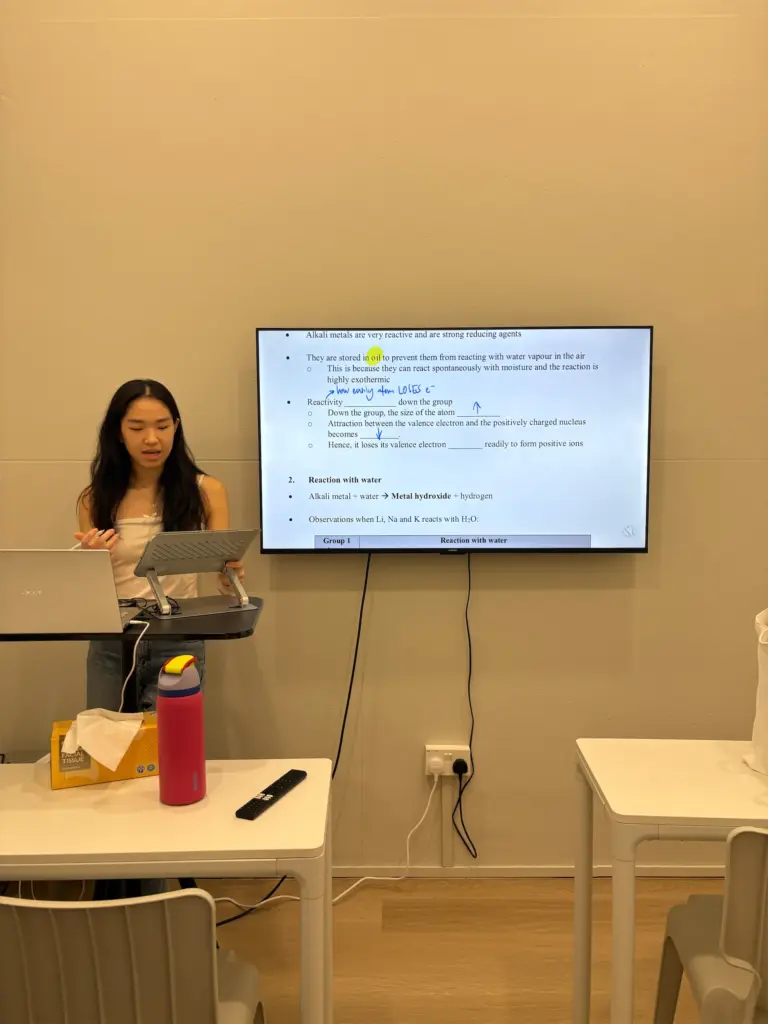 Young woman giving a presentation in a classroom with a digital screen.