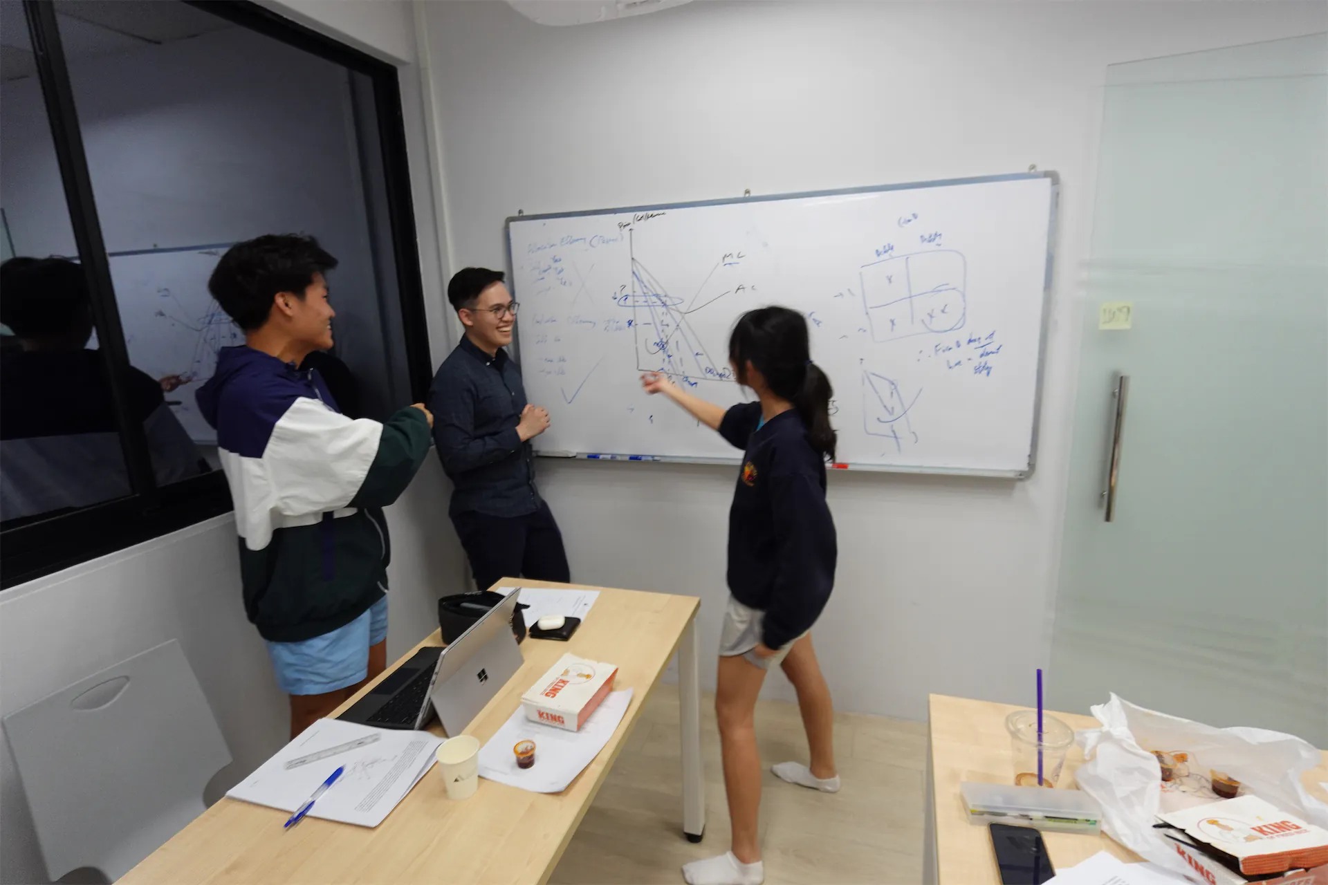 Students and teacher discussing on whiteboard in classroom.
