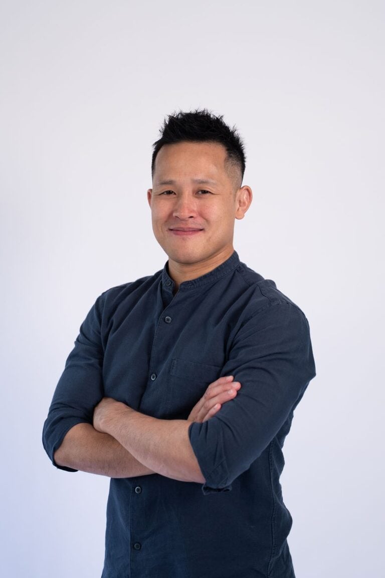 Confident Asian man in navy shirt with arms crossed against white background.