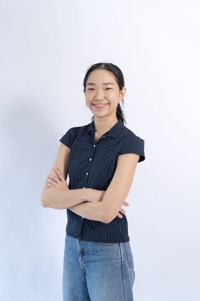 Smiling young Asian woman in casual attire with crossed arms.