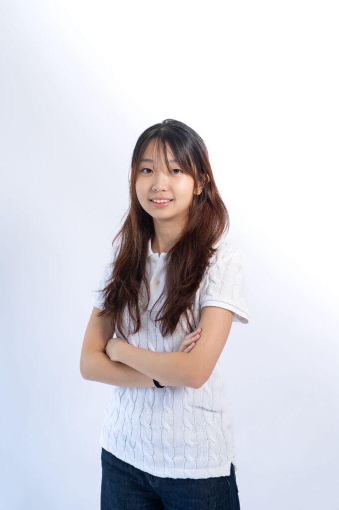 Young woman with long hair smiling and crossing arms against a white background.