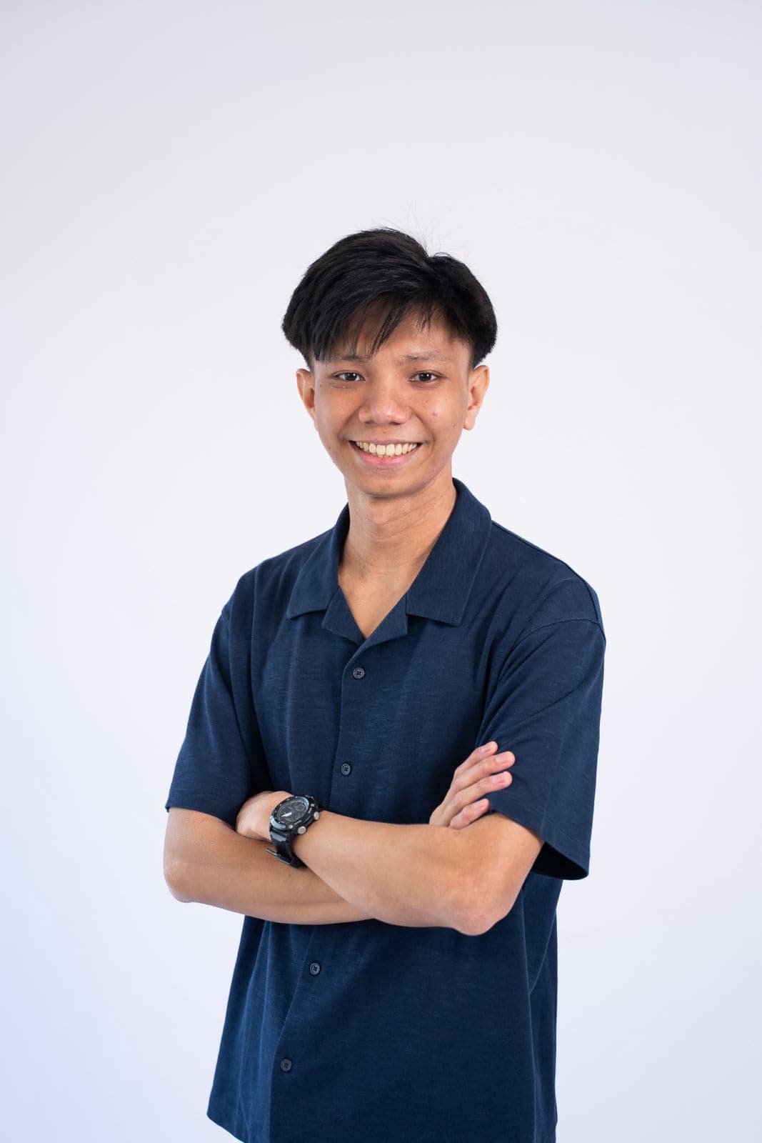 Young man smiling with arms crossed, wearing a navy blue shirt.