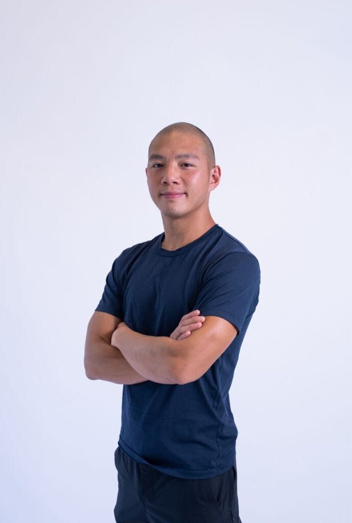 Confident young man with crossed arms in navy T-shirt against white background.