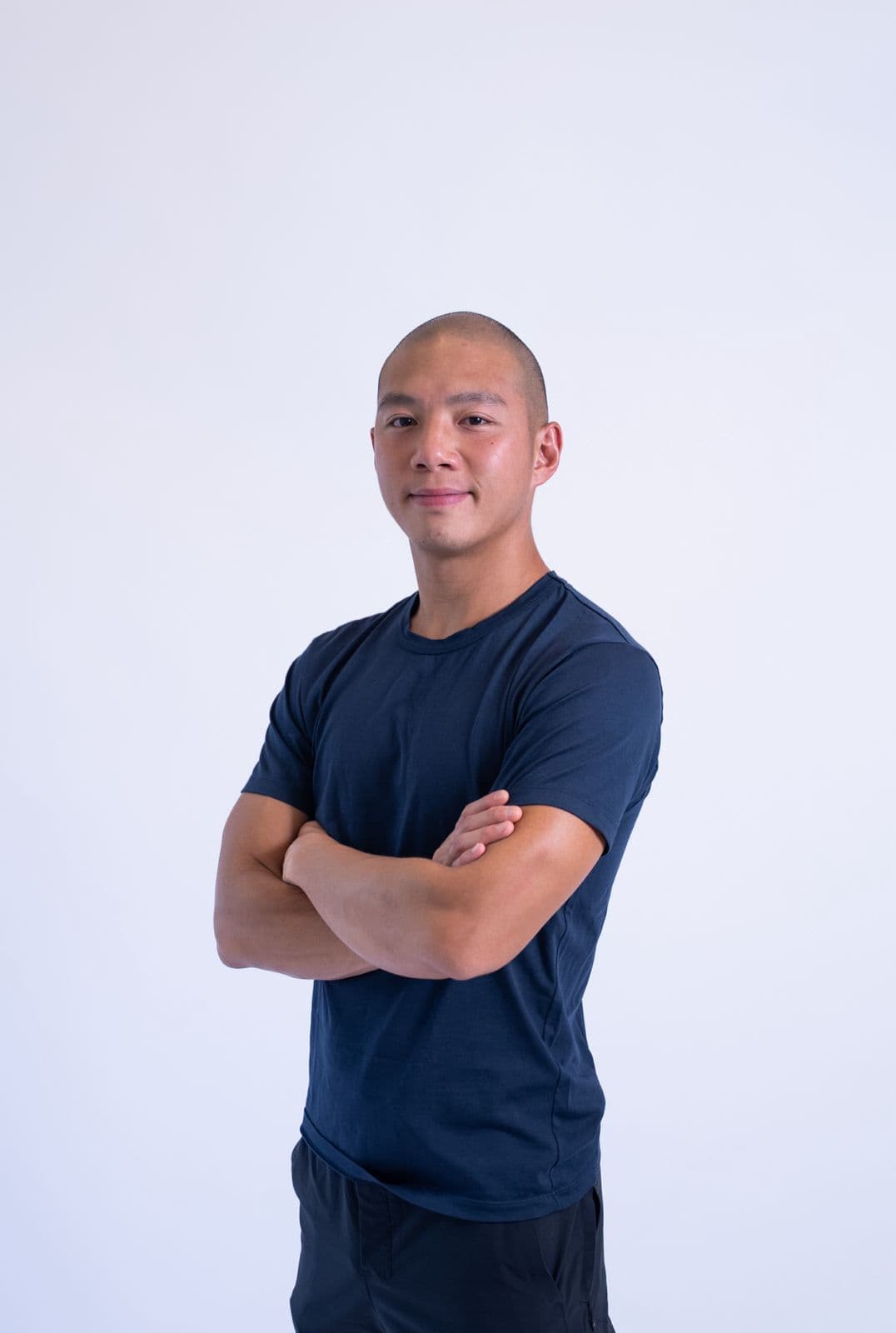 Confident young man with crossed arms in navy T-shirt against white background.