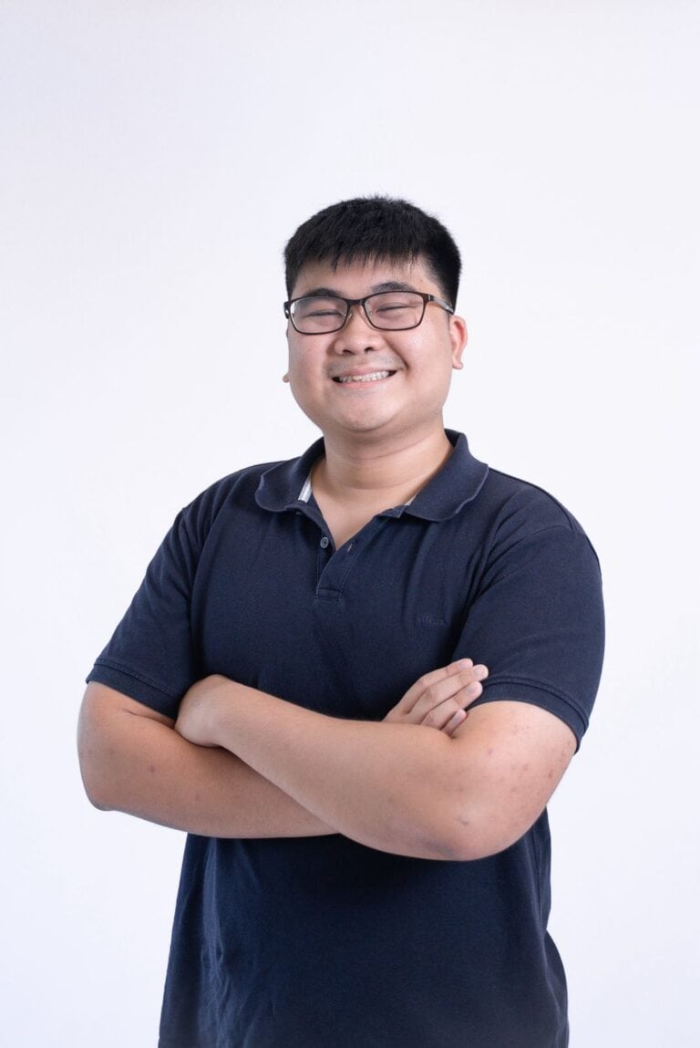 Smiling young man with glasses in a navy polo shirt against a white background.