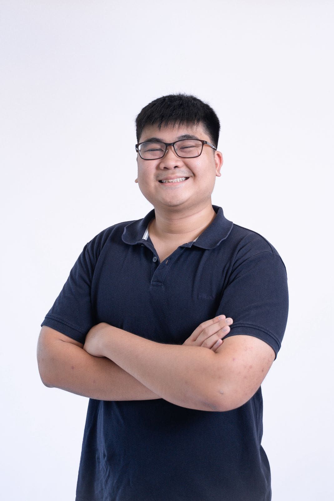Smiling young man with glasses in a navy polo shirt against a white background.
