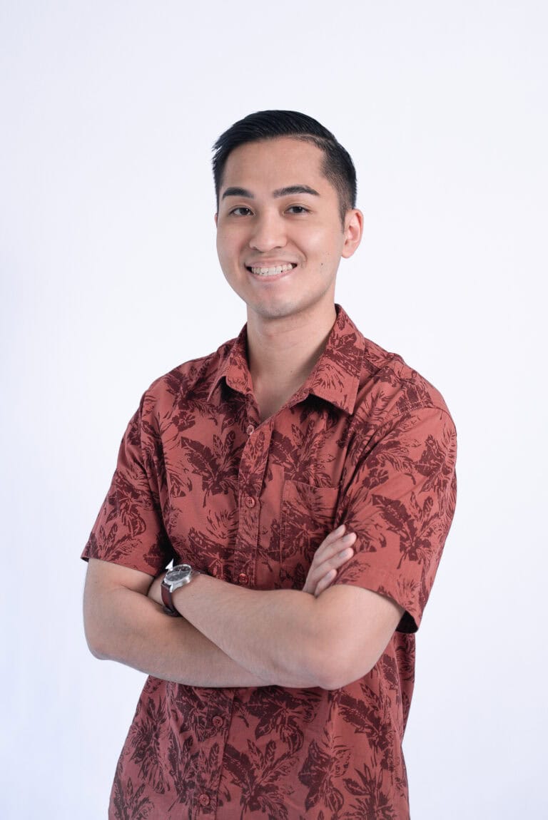 Smiling young man in a red floral shirt with crossed arms against a white background.