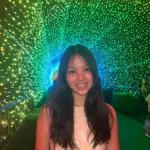 Young woman smiling under vibrant green and blue light display.