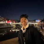 Smiling young man at night by the river in a cityscape setting.