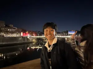 Smiling young man at night by the river in a cityscape setting.