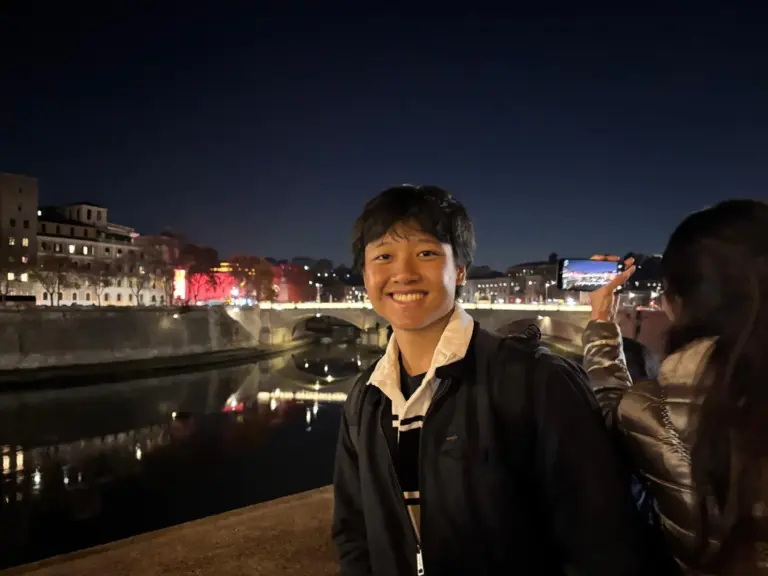 Smiling young man at night by the river in a cityscape setting.