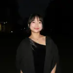 Young woman smiling outdoors at night, wearing a black dress and cardigan.