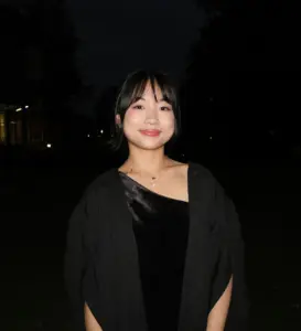 Young woman smiling outdoors at night, wearing a black dress and cardigan.