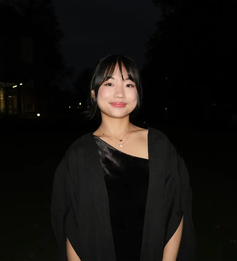 Young woman smiling outdoors at night, wearing a black dress and cardigan.