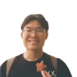 Young man with glasses smiling, holding a small snack, wearing a black T-shirt and backpack.
