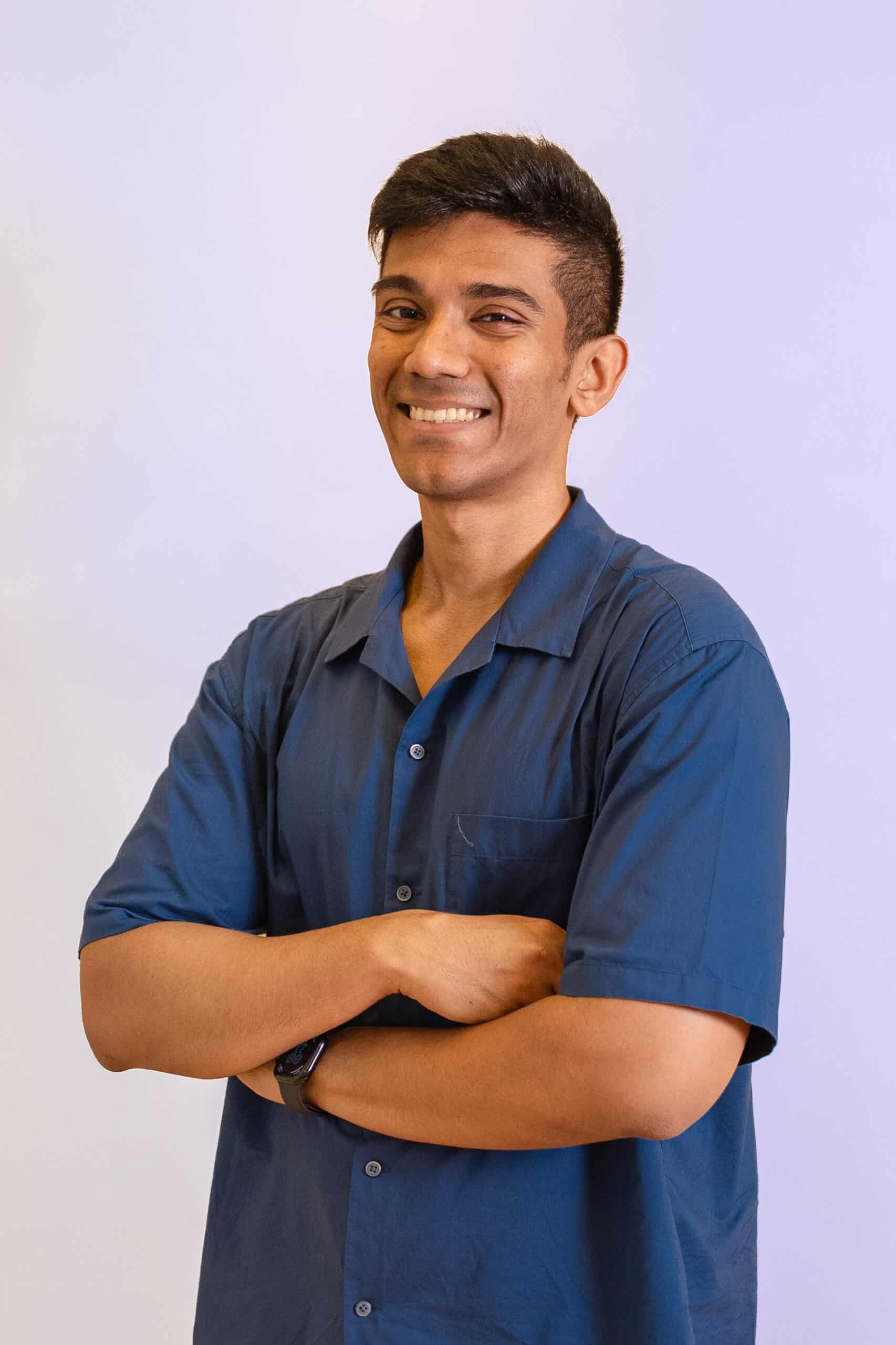 Confident young man in blue shirt smiling with arms crossed.