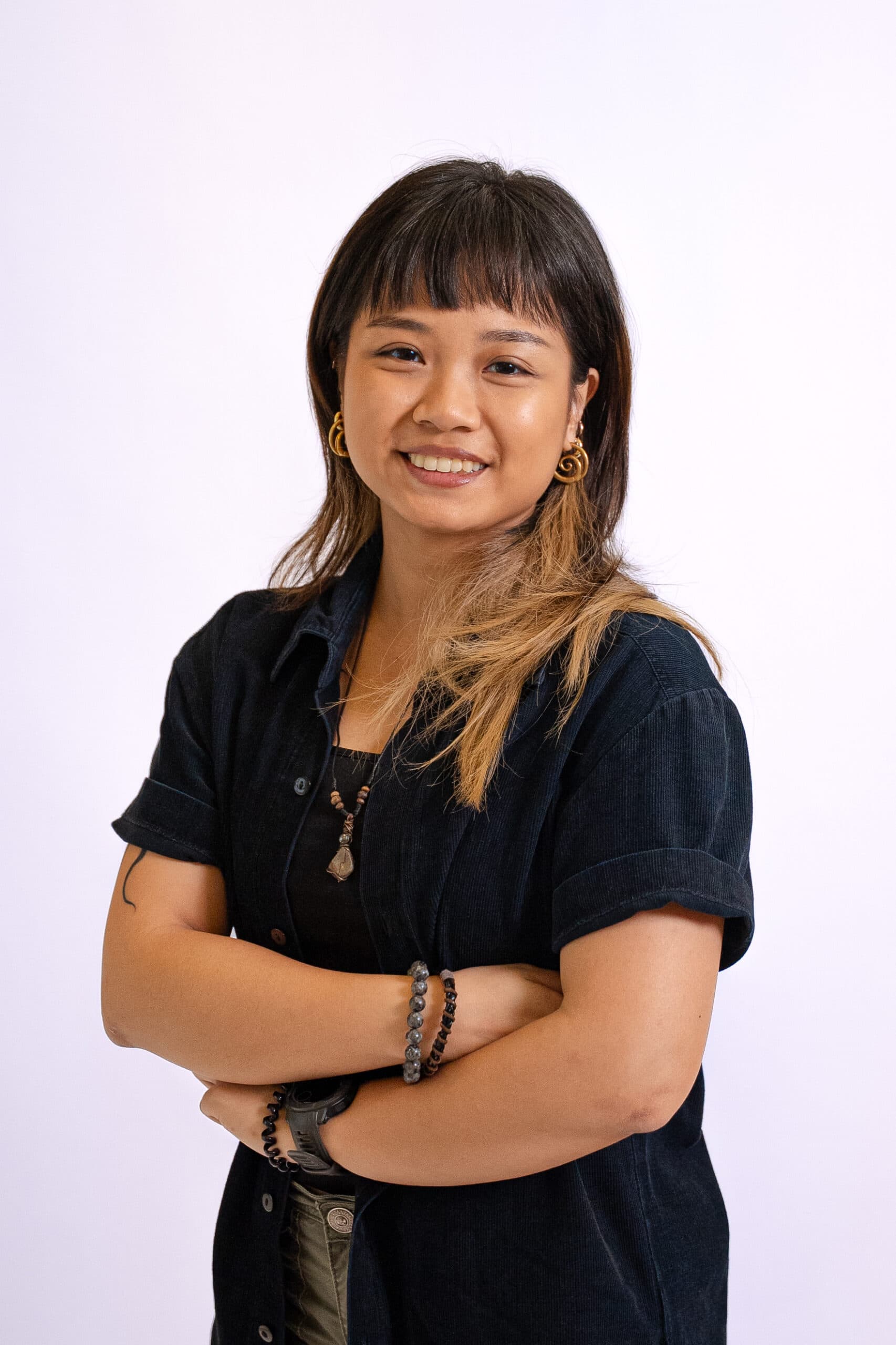 Smiling young woman with crossed arms, wearing a black shirt and accessories.